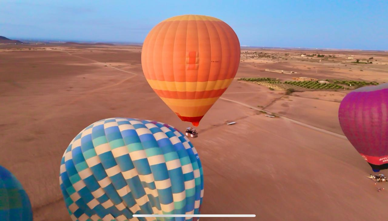 Orange, blue-checkered and pink hot air balloons flying over the countryside near Marrakech
