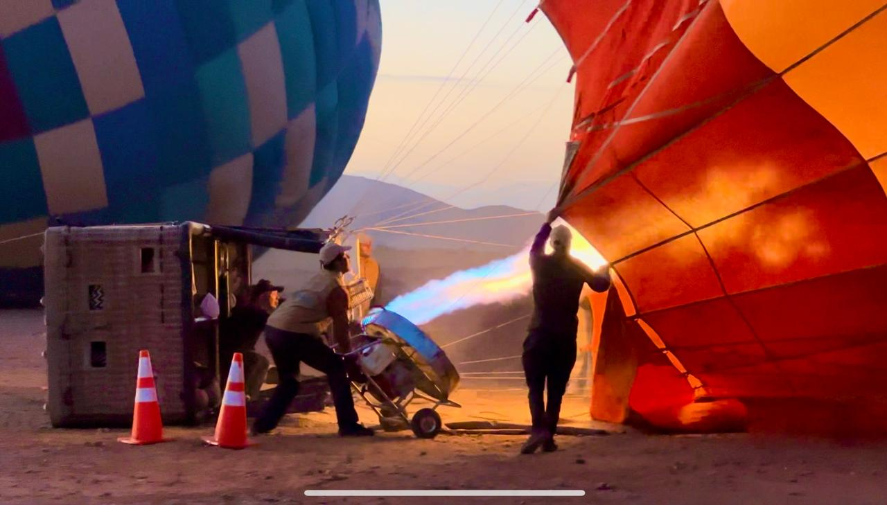 Crew using a burner to inflate a red hot air balloon envelope before a flight near Marrakech