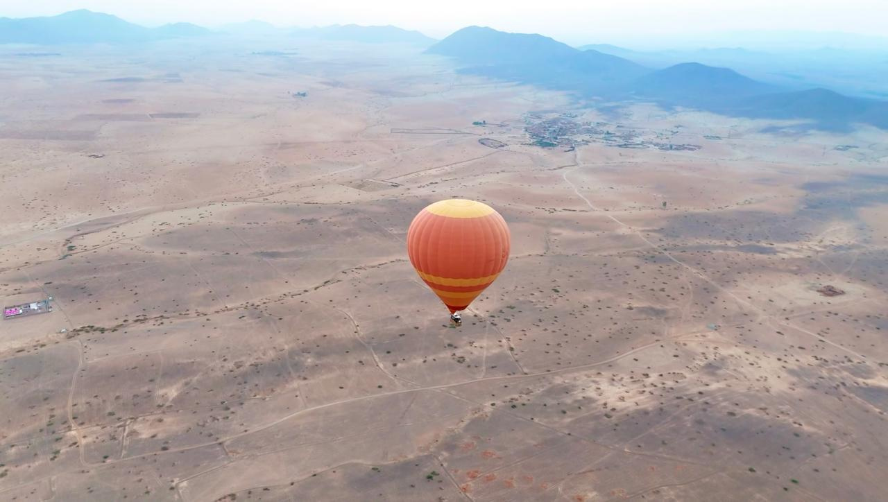 Hot air balloon ascending at dawn above the Moroccan desert plains with Atlas Mountains on the horizon