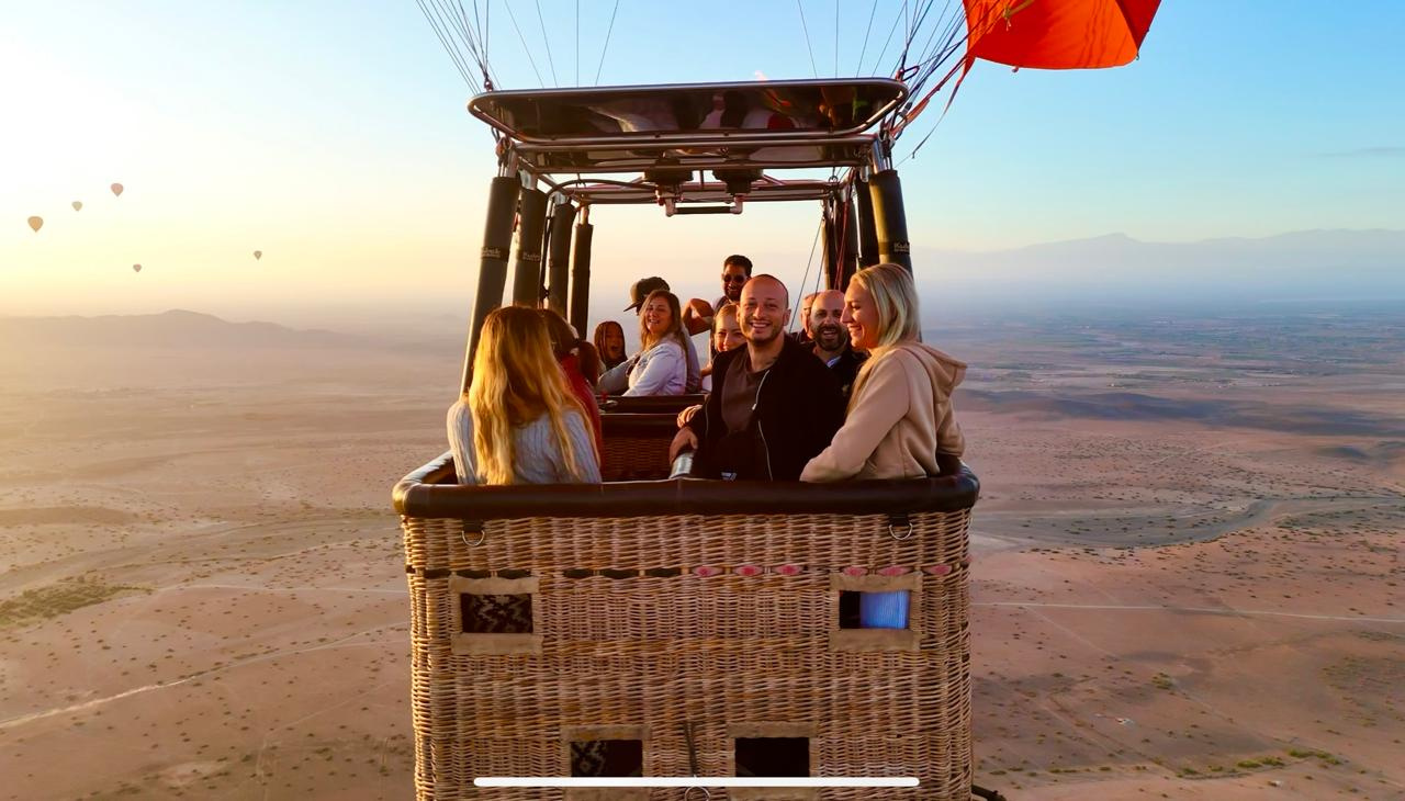 Smiling passengers enjoying the view from a hot air balloon basket above Marrakech