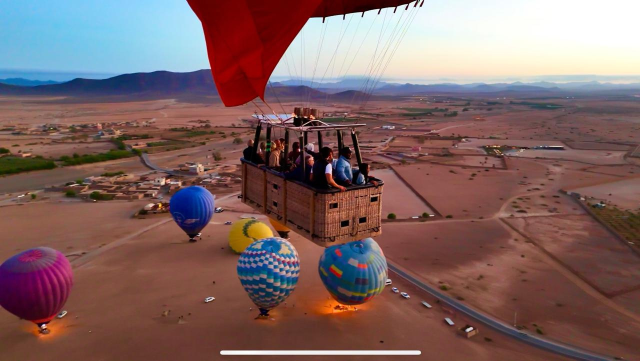 Wicker balloon basket with passengers flying above blue, yellow and patterned balloons near Marrakech