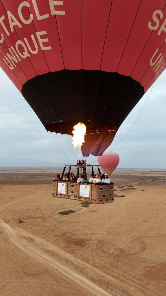 Bright burner flame firing above a passenger basket beneath a red and black hot air balloon near Marrakech