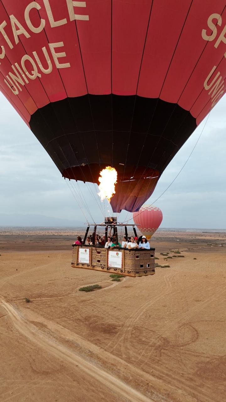 Bright burner flame firing above a passenger basket beneath a red and black hot air balloon near Marrakech