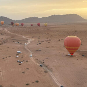 Several hot air balloons spread across a dry landscape with a winding road below near Marrakech
