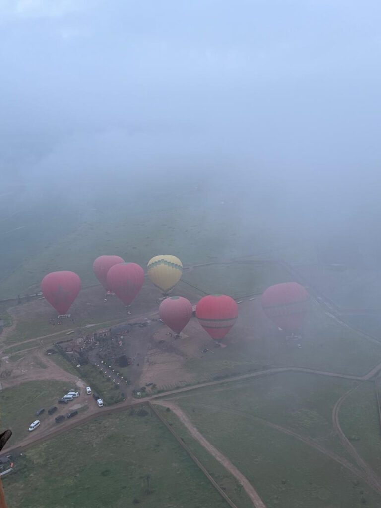 Several hot air balloons viewed from above through morning mist over rural land near Marrakech