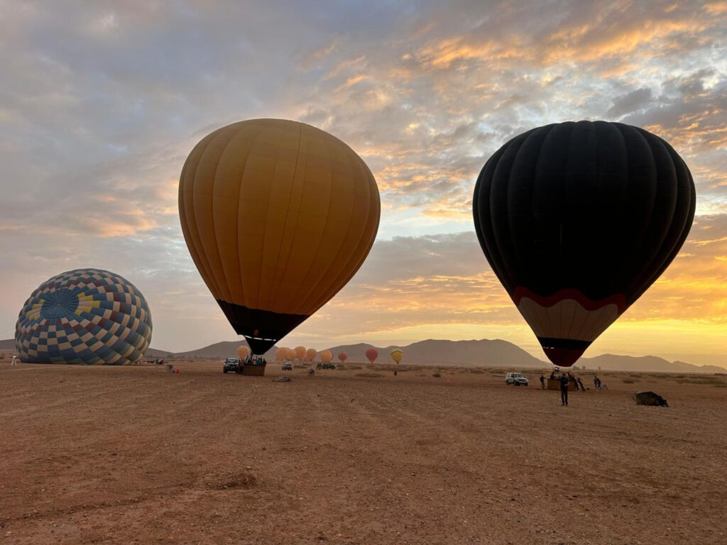 Yellow, black and patterned hot air balloons fully inflated on an open field at sunrise near Marrakech