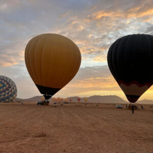Yellow, black and patterned hot air balloons fully inflated on an open field at sunrise near Marrakech