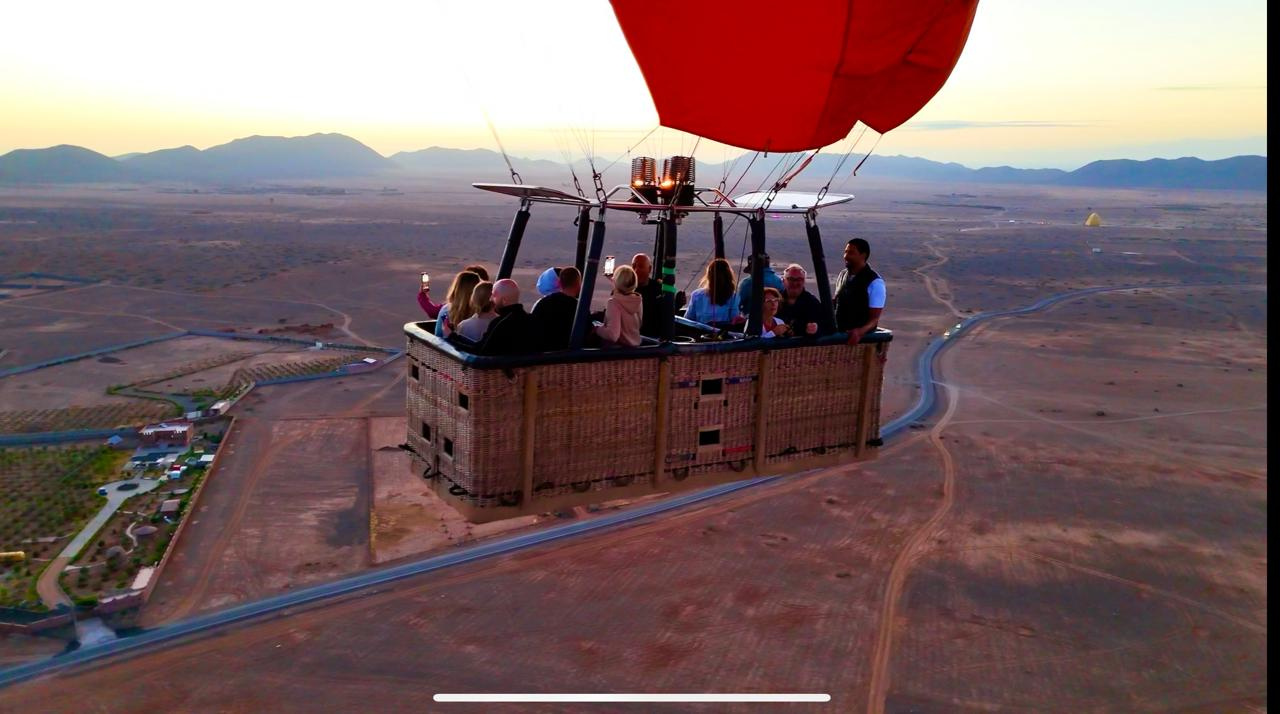 Close side view of passengers in a wicker hot air balloon basket above roads and countryside near Marrakech