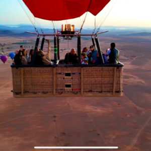 Front view of passengers inside a wicker hot air balloon basket flying over rural land near Marrakech