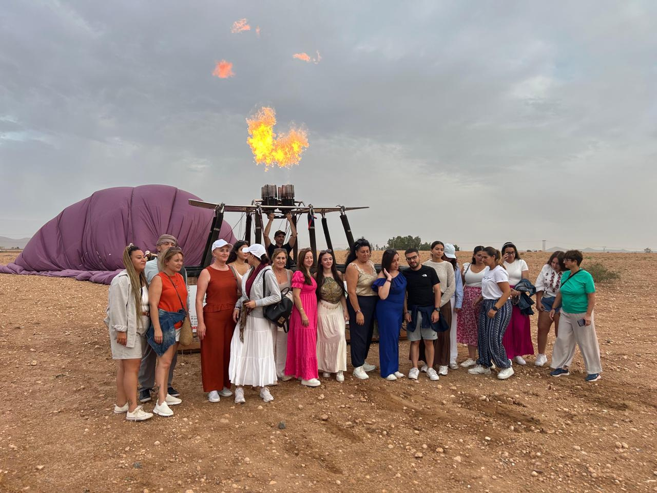 Large travel group posing beside a deflated purple hot air balloon envelope after a flight near Marrakech