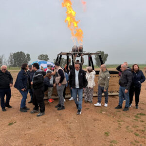 Travel group posing beside a balloon basket as a large burner flame rises behind them near Marrakech