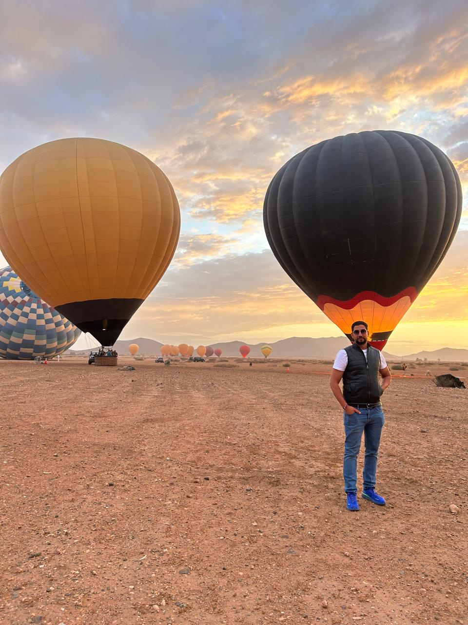 Traveler standing on a launch field beside several fully inflated hot air balloons near Marrakech
