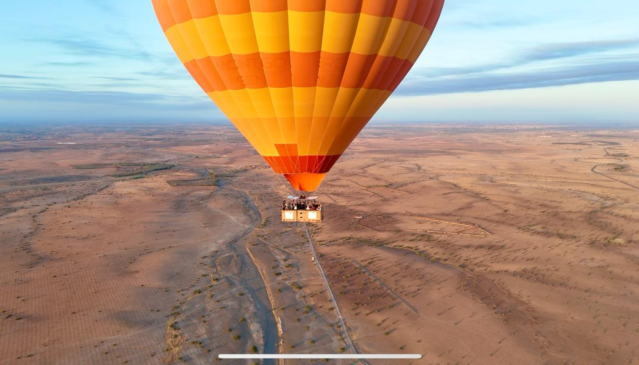 Aerial view looking down on a large orange hot air balloon over tan countryside near Marrakech