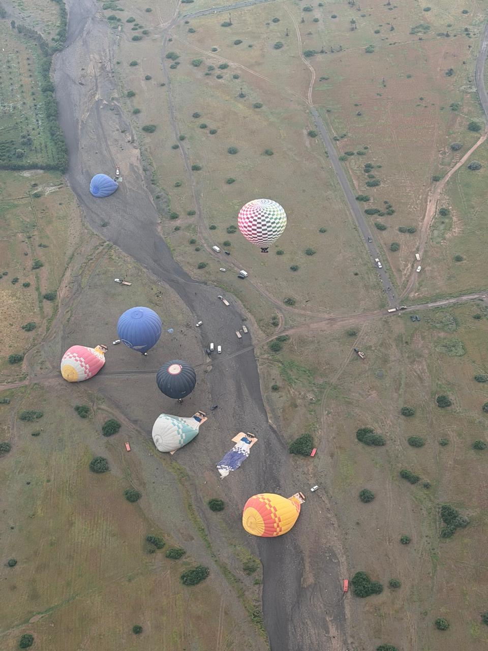 Top-down aerial view of several colorful hot air balloons scattered across countryside near Marrakech