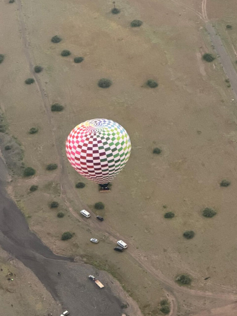 Top-down view of a green and white checkerboard hot air balloon with vehicles and tracks below near Marrakech